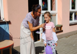 na tarasie dziewczynka z fioletowym balonem mówi do mikrofonu, który trzyma nauczycielka